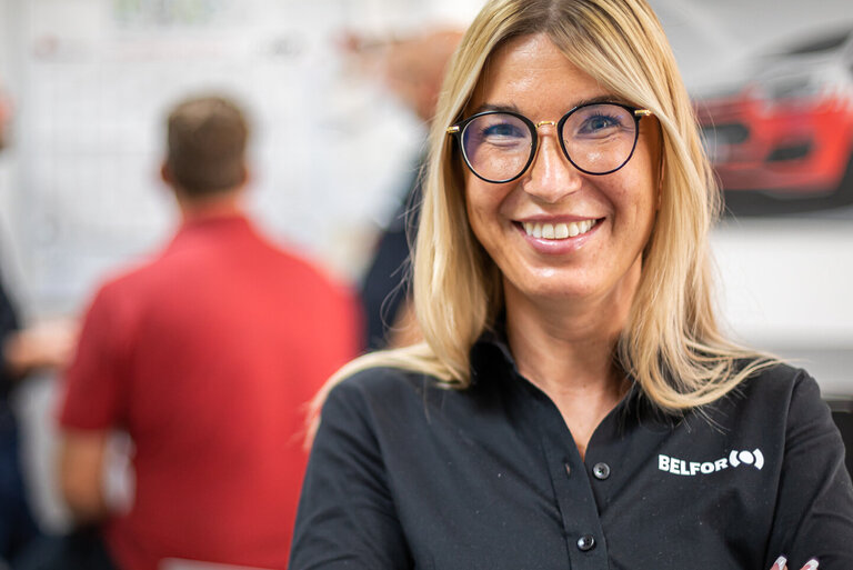 " BELFOR Mitarbeiterin im Büro lächelt in die Kamera."